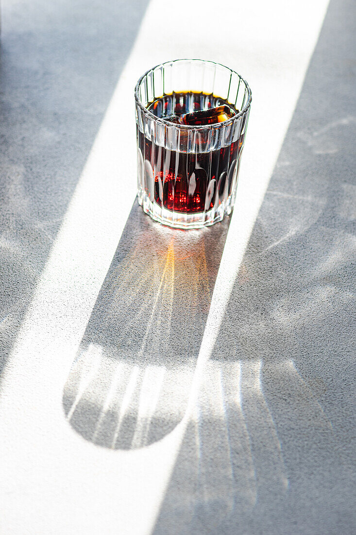 Ein mit Kirschlikör gefülltes Glas wirft einen langen Schatten auf eine vom Sonnenlicht beleuchtete, strukturierte Oberfläche