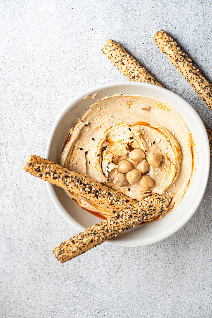 Top view of healthy plant-based plate with hummus and bread sticks served in a bowl against gray background