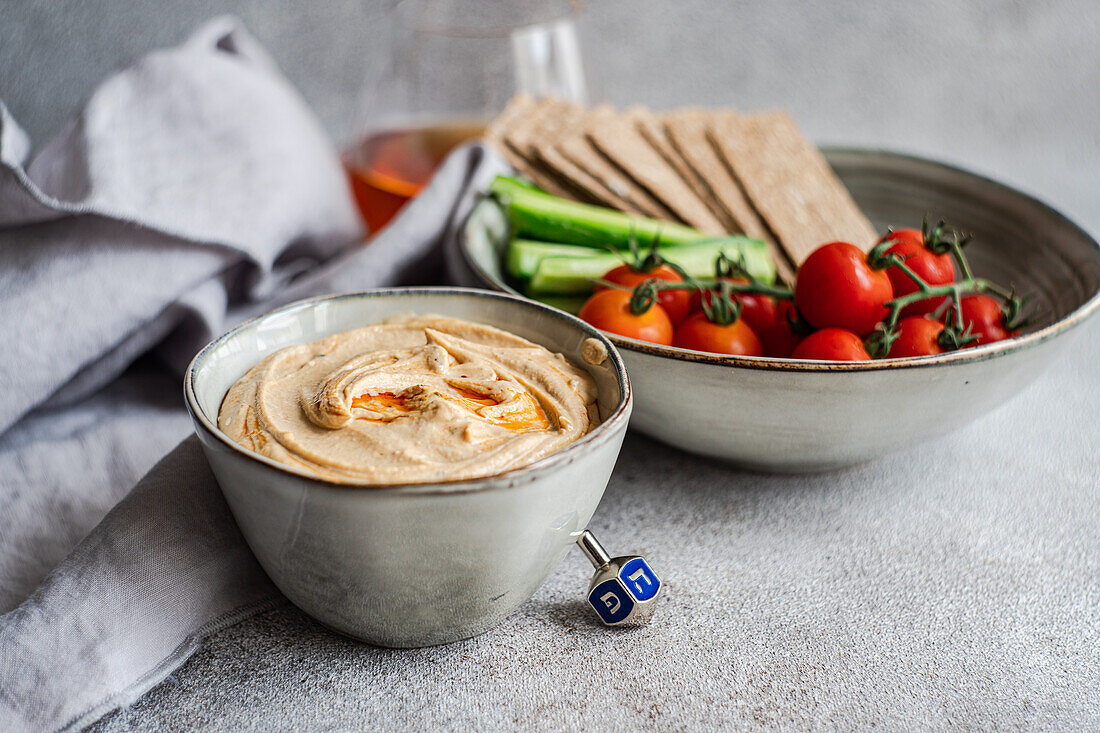 High angle of healthy plant-based plate with hummus and vegetables served in bowls near napkin and glass of liquor against blurred background