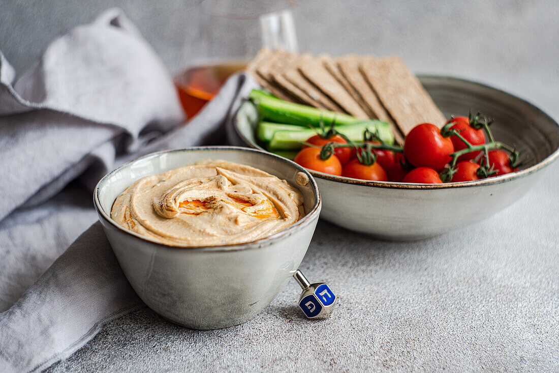 Hoher Winkel eines gesunden Pflanzentellers mit Hummus und Gemüse, serviert in Schalen neben einer Serviette und einem Glas Schnaps vor grauem Hintergrund