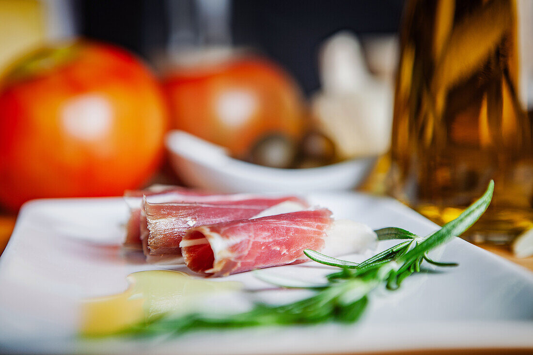 Close-up of appetizing iberian ham slices with fresh mozzarella cheese and rosemary on a white plate.