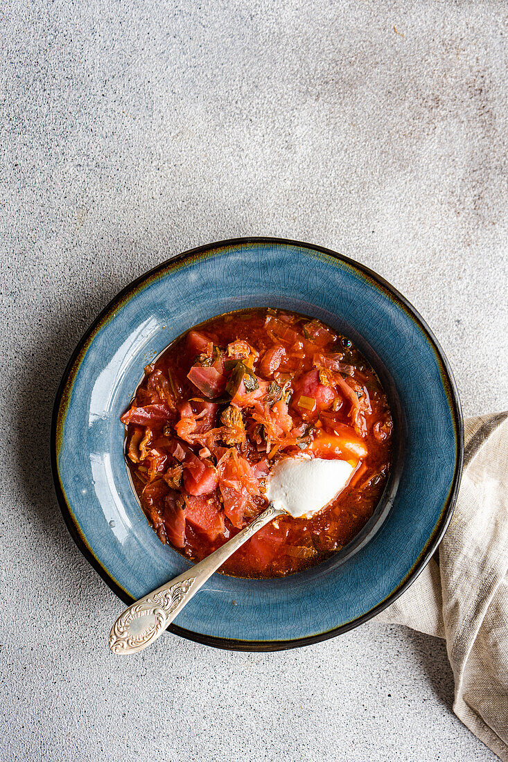 Top view of bowl with traditional Ukrainian soup borscht served in blue ceramic bowl on gray surface and white sour cream sauce