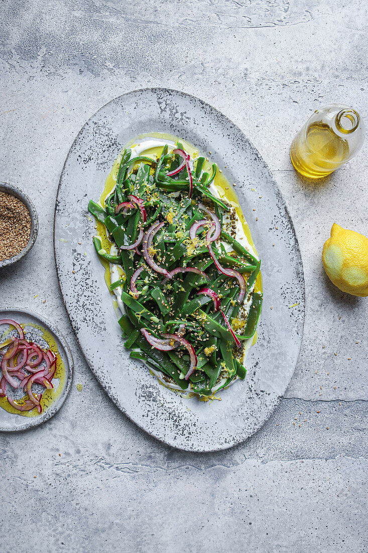 Draufsicht auf einen appetitlichen vegetarischen Salat mit grünen Kräutern und Zwiebelscheiben, der auf einem Teller mit Öl serviert und mit Zitronenschalen garniert wird