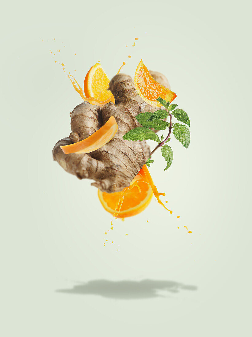 Fliegender Ingwer mit Orangenscheiben und Saft spritzt auf blassgrünen Hintergrund Minzblätter. Zutaten für erfrischende Sommergetränke. Kreatives Konzept für schwebende Lebensmittel und Getränke. Frontansicht