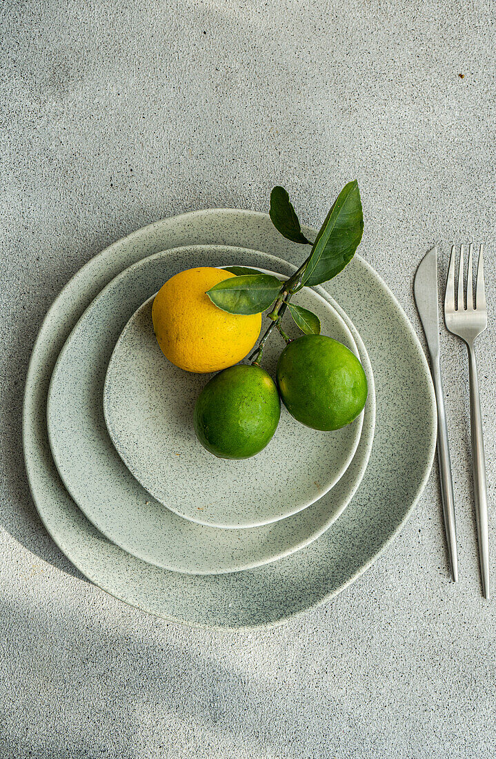 Draufsicht auf gestapelte Keramikteller mit einer Zitrone und zwei Limetten, die moderne Küchenästhetik mit natürlichen Elementen verbinden