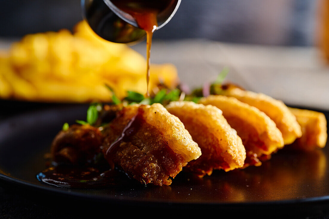 Cook preparing traditional Ecuadorian dish pouring sauce on appetizing fried breaded meat served on plate against blurred background
