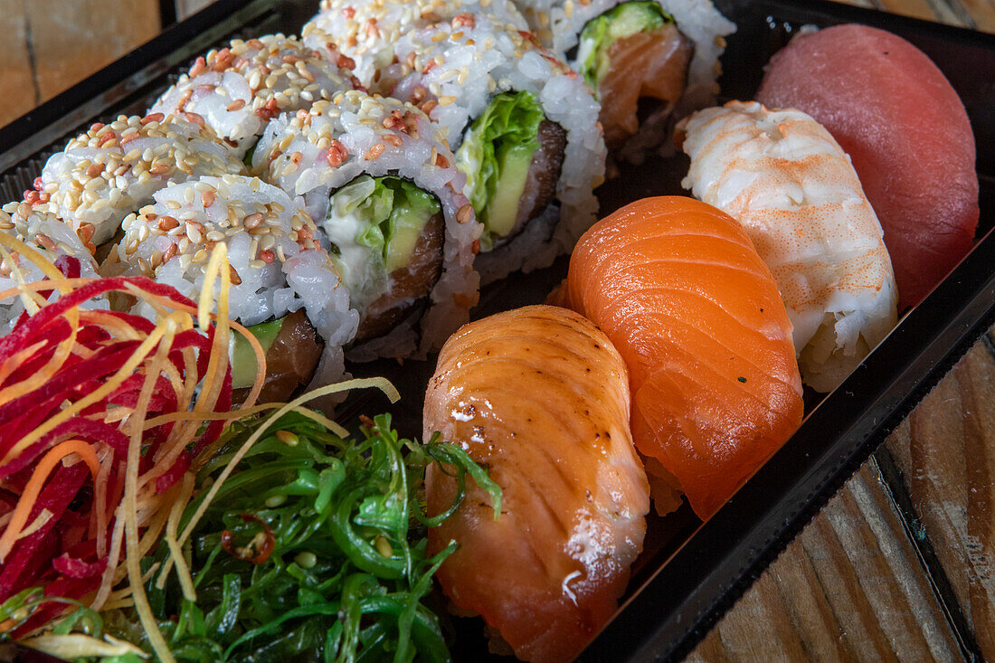 Schwarzer Plastikbehälter für Uramaki-Thunfisch-Sushi-Rollen und Nigiri-Sushi mit verschiedenen Fischsorten und Seetang-Salat