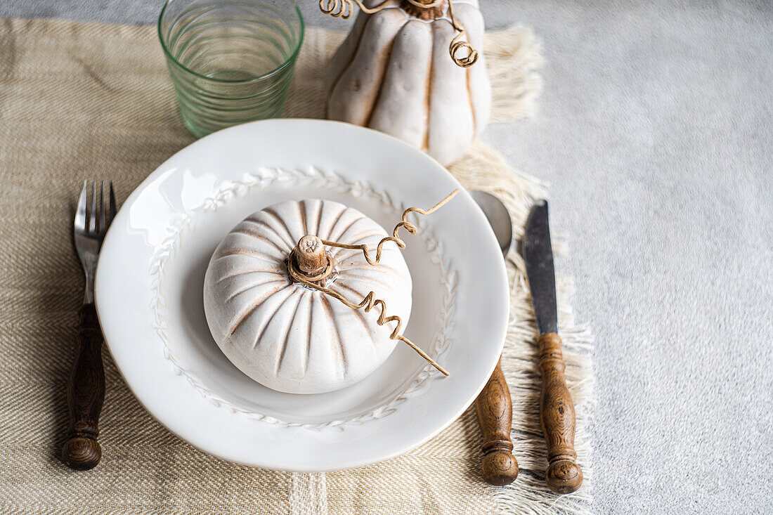 High angle of autumnal table setting with white pumpkin on plate placed on table near cutlery and glass