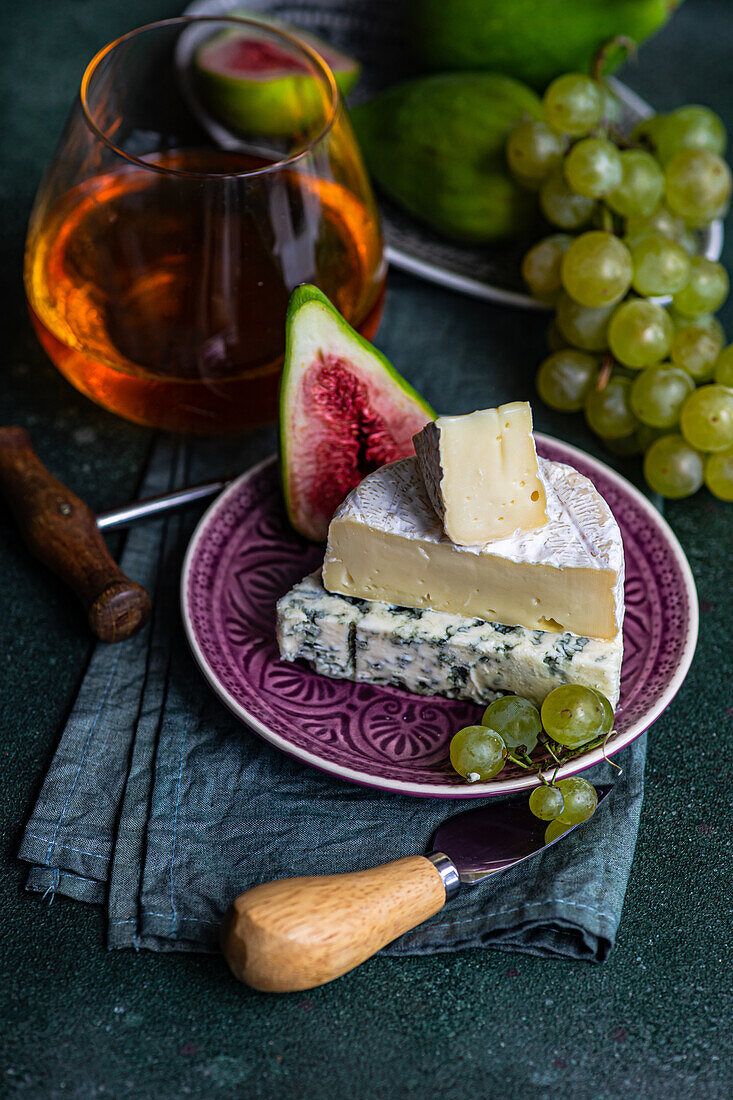 Assorted yummy snacks with cheese and served on plate placed with grapes and figs and drink