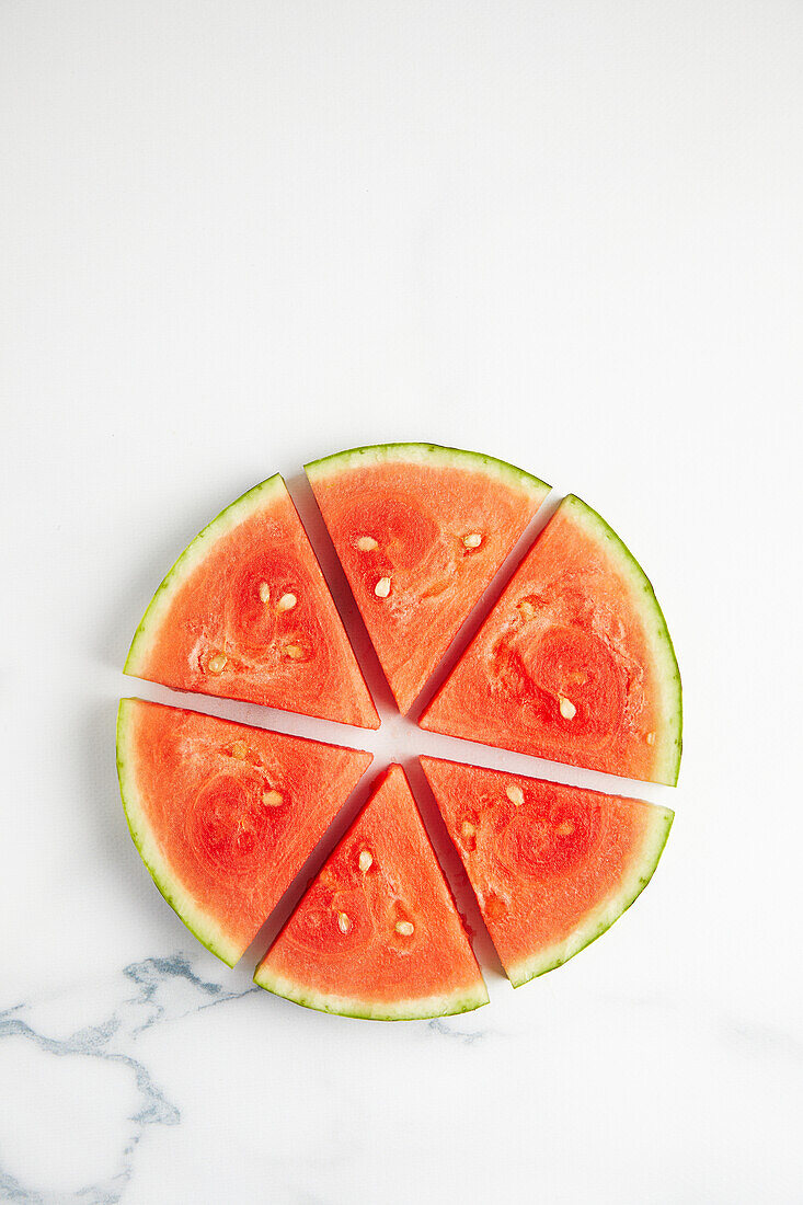 Draufsicht auf Scheiben einer saftigen Wassermelone mit Kernen auf einer weißen Keramikfläche