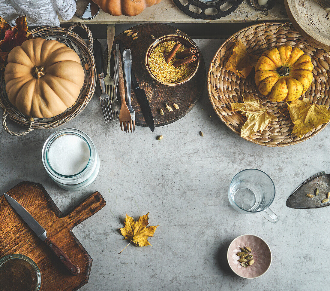 Herbstlicher Lebensmittelhintergrund mit Kürbissen, Schneidebrett und Messer, verschiedenen Gewürzen und Küchenutensilien. Ansicht von oben