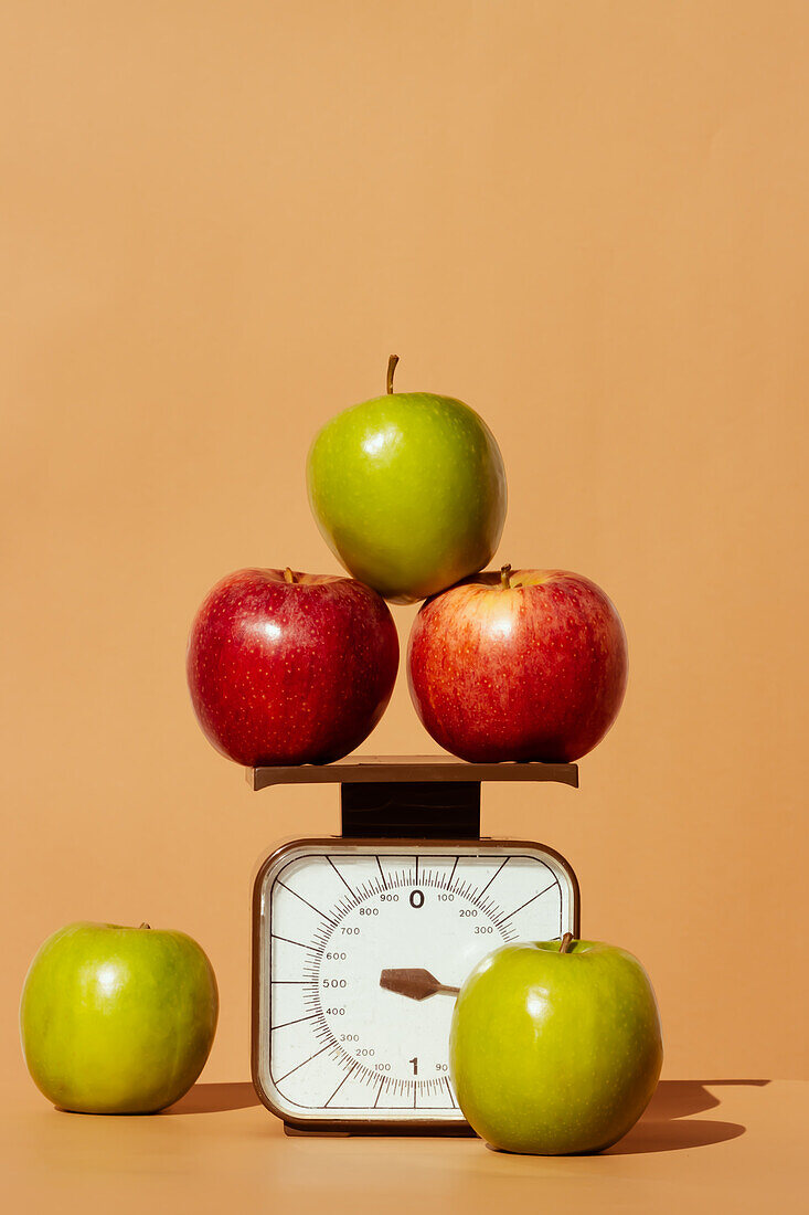 Fresh and juicy red and green apples on weighing scale as part of healthy calorie controlled diet on colored background