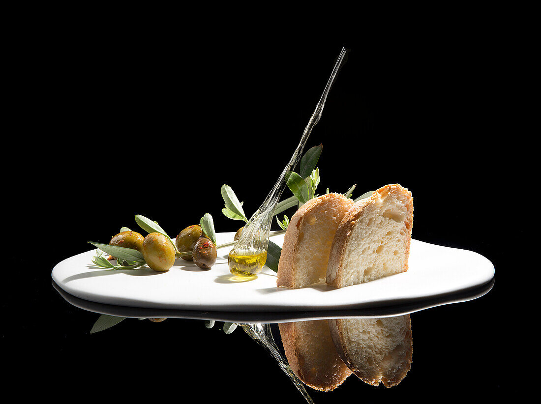 Exquisite bread toasts served on white plate with green herbs and olives with oil against against black background