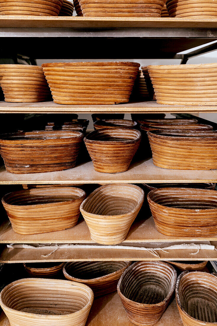 Various wooden brown proofing baskets for baking bread and pastry items arranged on shelves in kitchen at bakehouse