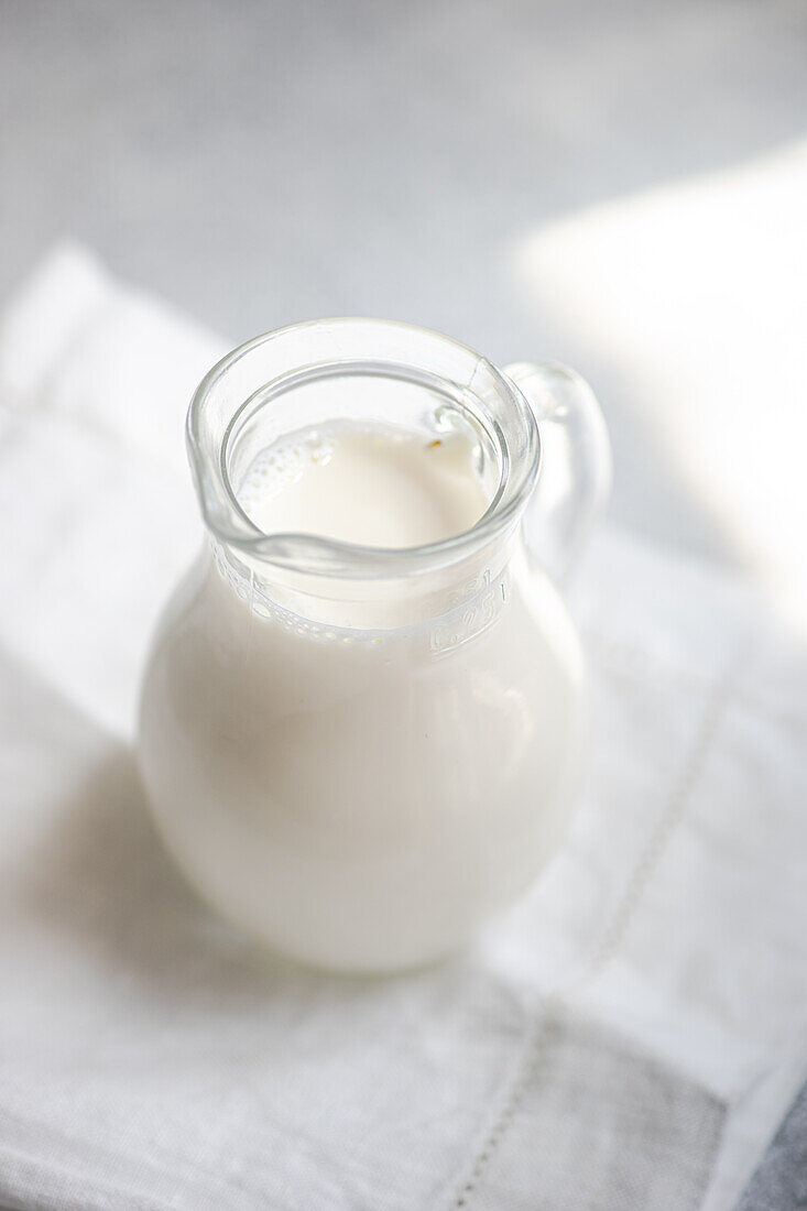 High angle of white raw cow milk in glass jar placed on white napkin against blurred background