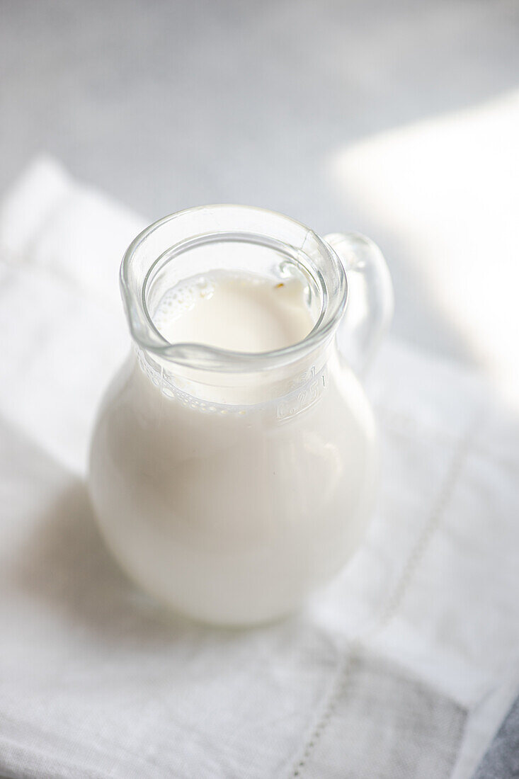 Hoher Winkel von weißer roher Kuhmilch in einem Glasgefäß auf einer weißen Serviette vor einem unscharfen Hintergrund