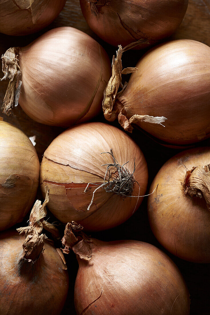 A high-resolution image showcasing a pile of ripe onions with their papery skins on a rustic wooden background