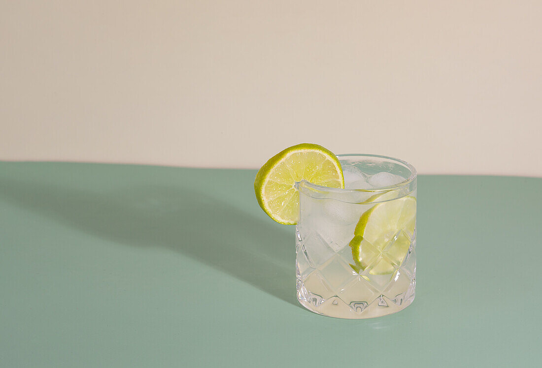 Vorderansicht eines funkelnden transparenten Glases mit erfrischendem Cocktail und Zitrusscheiben auf einem Tisch vor weißem Hintergrund