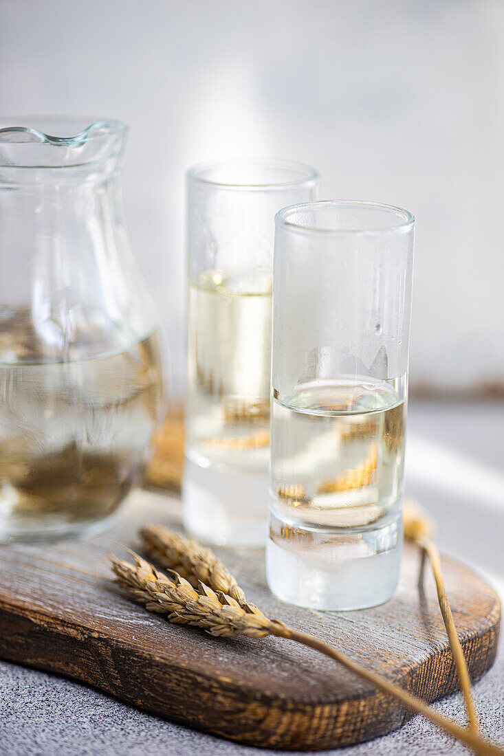 Traditionelles ukrainisches alkoholisches Getränk aus Weizen, bekannt als Gorilka, serviert in einem transparenten Glas und Gläsern auf einem Schneidebrett vor einem unscharfen Hintergrund
