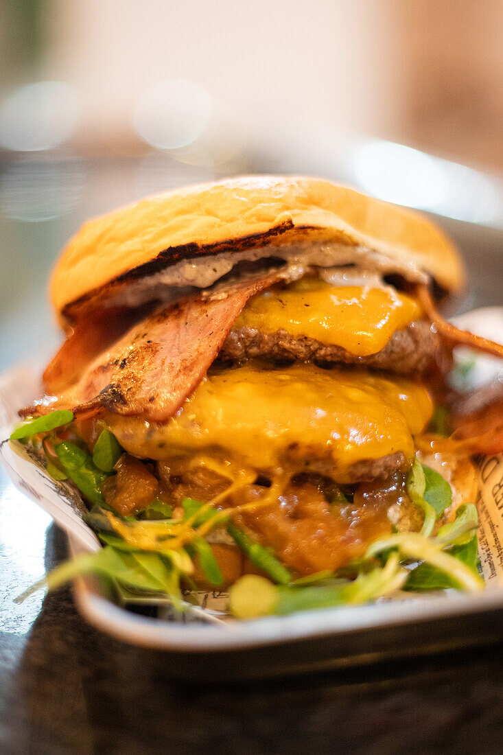 Gourmet beef burger with melted cheddar, crispy bacon, caramelized onions, and fresh greens on a brioche bun, served on a newspaper-lined plate