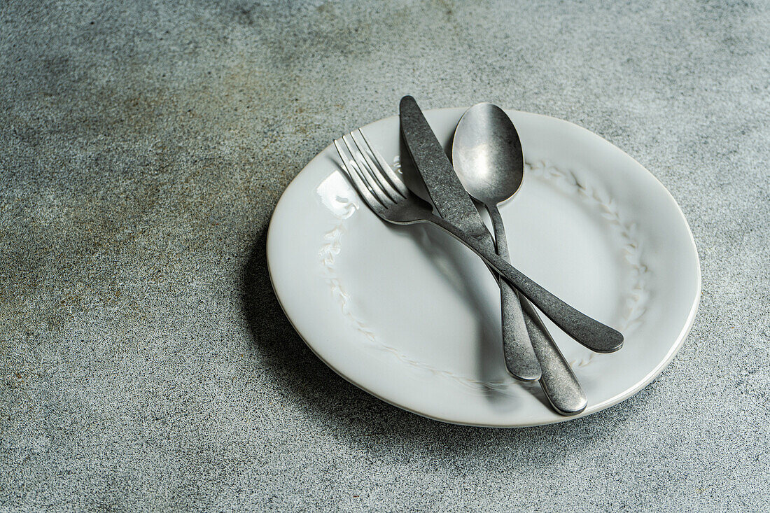 High angle of vintage cutlery set placed on white plate against gray surface in light kitchen