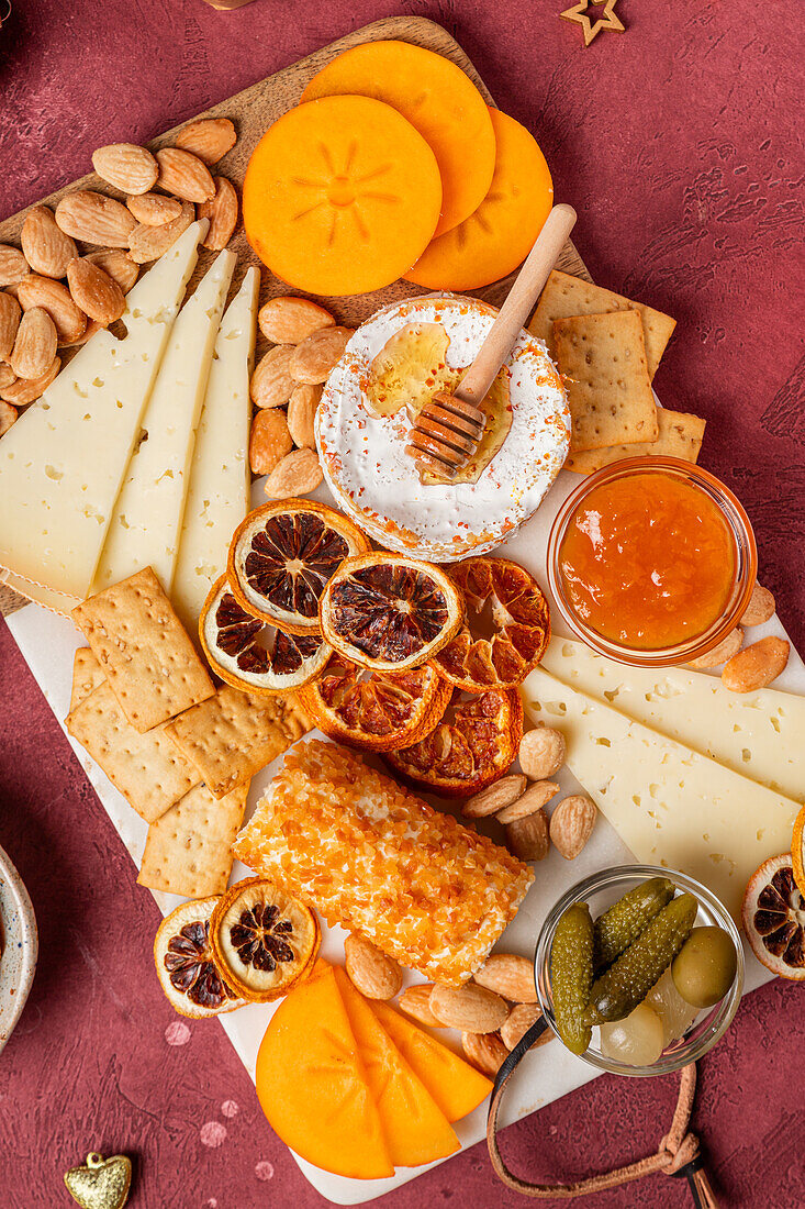 An appetizing cheese platter featuring a variety of cheeses, almonds, honeycomb, crisp crackers, sliced persimmon, and dried citrus, perfect for entertaining.