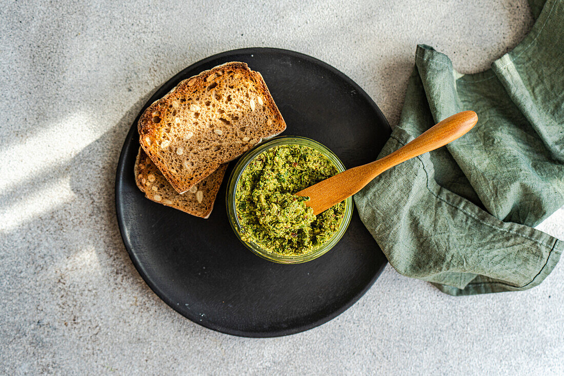 Top view of homemade tasty bread and pesto sauce with wooden spoon placed on gray table near napkin