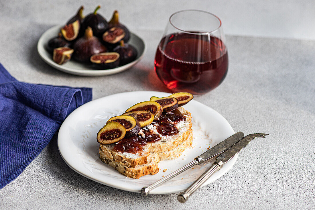 A gourmet toast topped with figs and jam, paired with a glass of red wine, presented on a white plate for a sophisticated snack.