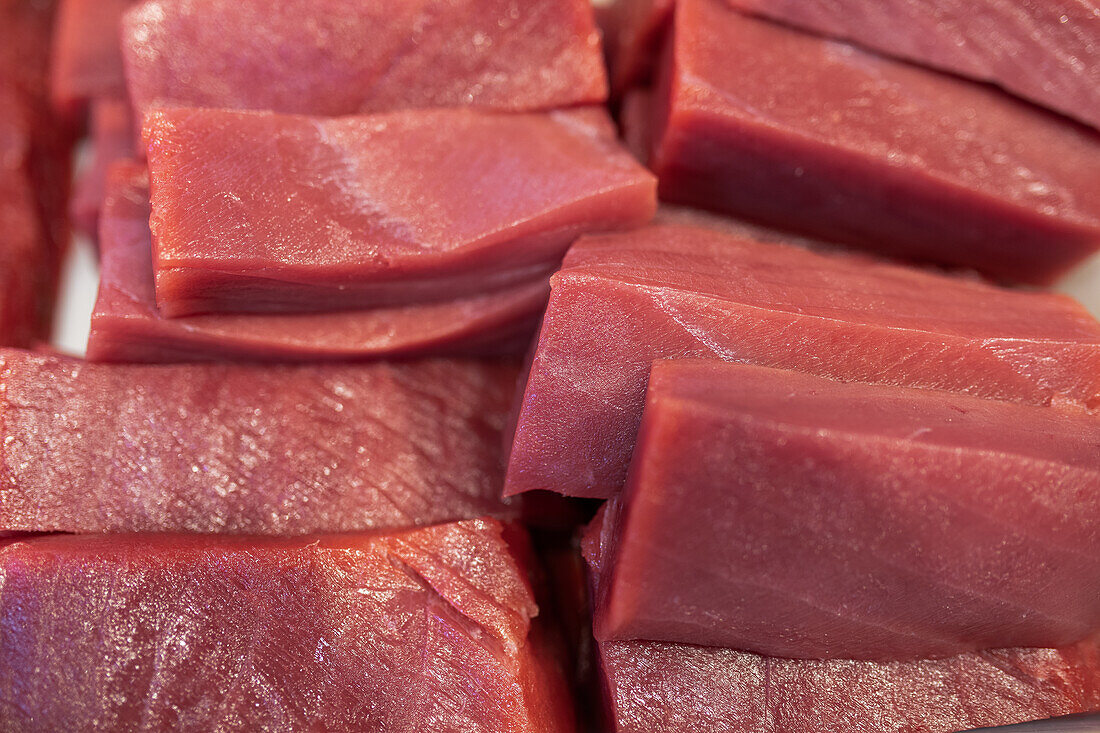 Closeup view of freshly cut pieces of raw red meat stack together over surface in bright kitchen