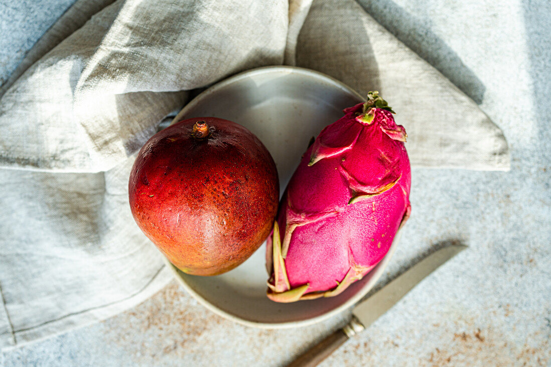 Lebendige Drachenfrucht und Mango neben einem Messer auf einem Keramikteller vor einem rustikalen Stoffhintergrund