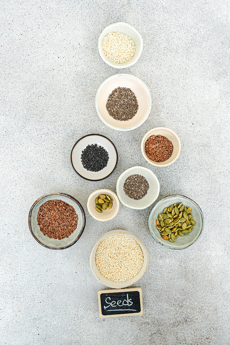 Top view of various seeds in bowls on a concrete background, labeled with a 'Seeds' chalkboard sign in a christmas tree shape