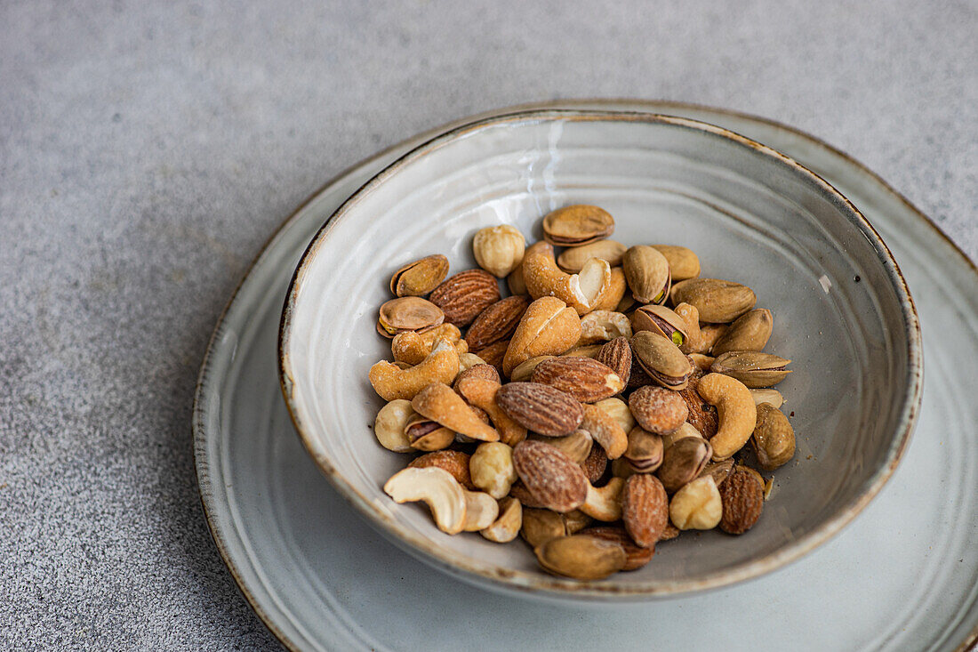 A variety of mixed nuts presented in a clear glass bowl set against a neutral gray backdrop, perfect for a healthy snack