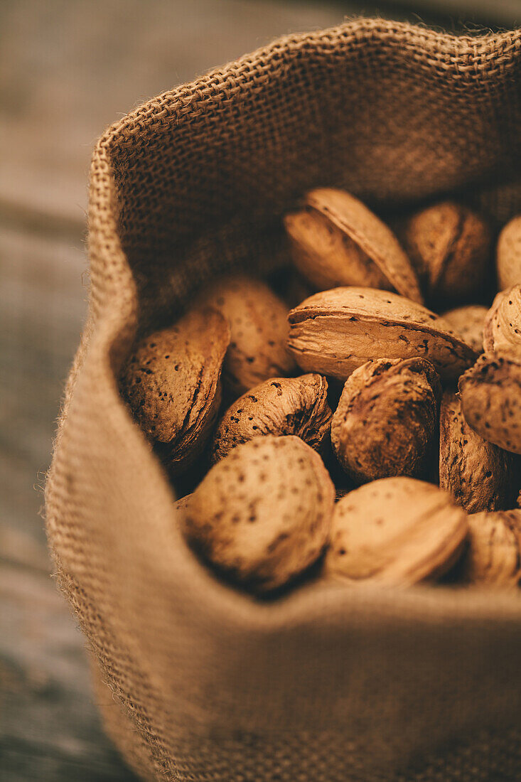 Close-up of a burlap sack overflowing with fresh almonds, set on a rustic wooden background