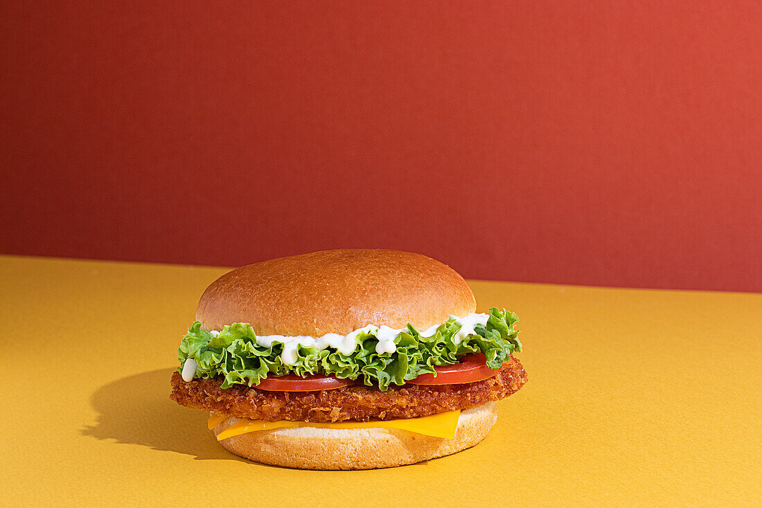 Leckerer Fisch-Burger mit Tomaten, Käsescheiben und frischem Salat auf gelbem und rotem Hintergrund