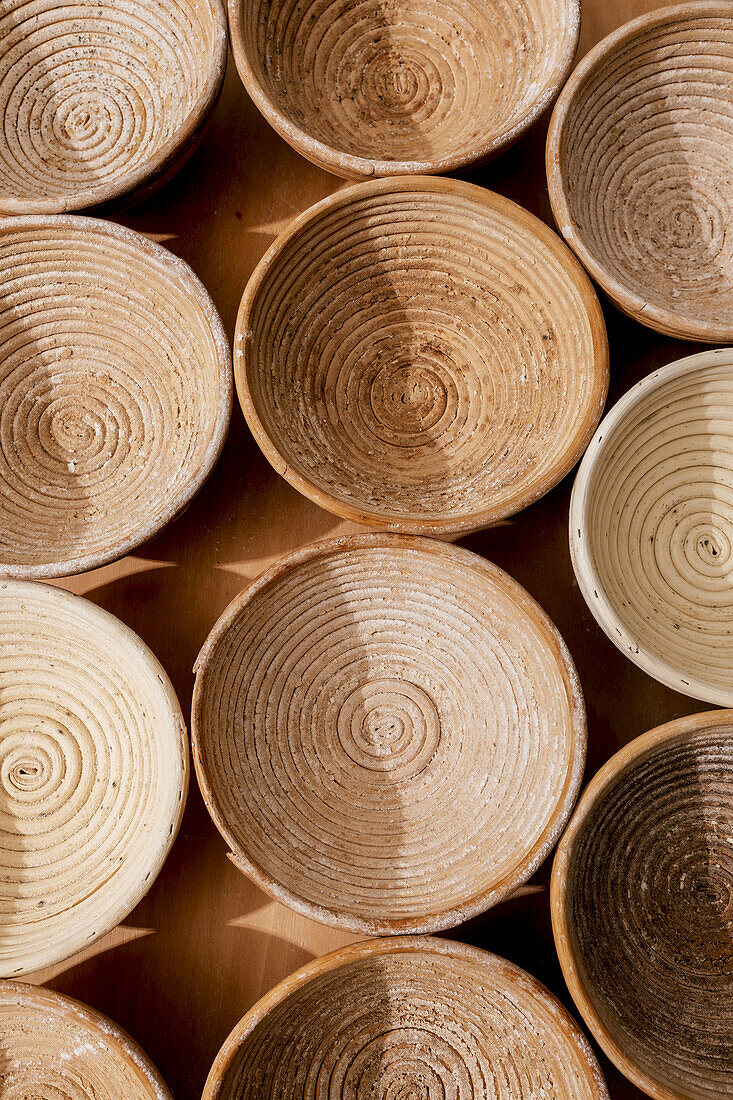 Blick von oben auf braune, runde Gärkörbe aus Holz zum Brotbacken, die auf einem Tisch in der Küche einer Bäckerei stehen