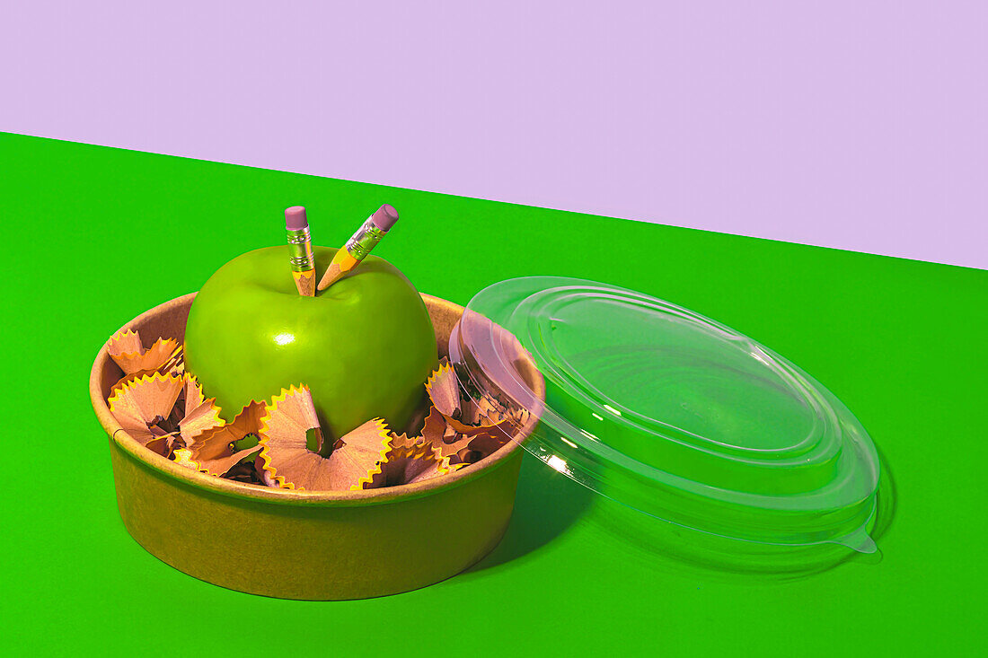 Gesunde Äpfel von oben, umgeben von Bleistiftspänen in einer Lunchbox auf grünem und weißem Hintergrund, die das Konzept des Null-Abfalls darstellt
