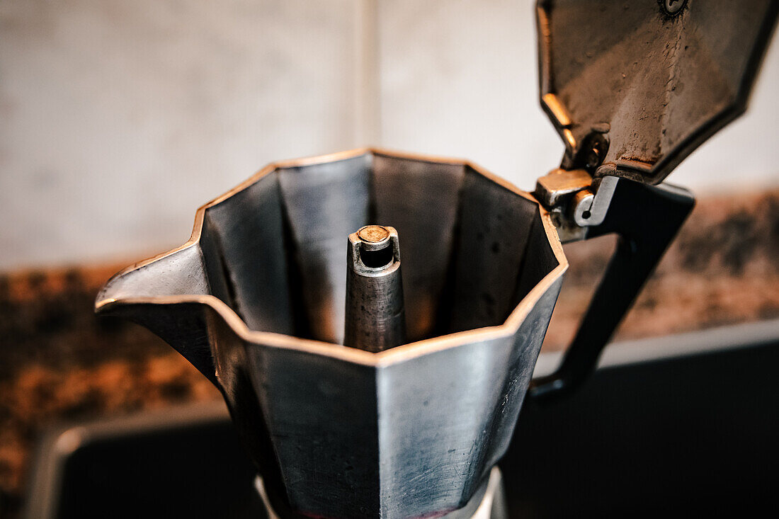 Close-up of stainless steel stovetop espresso maker placed on sleek cooktop with an ornate tiled backsplash providing a contrasting backdrop emphasizing the allure of home brewed Italian coffee