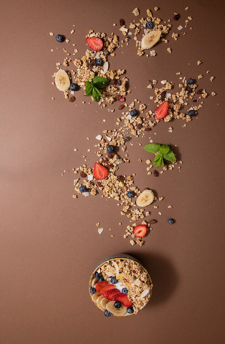 Schale mit leckerem Müsli und frischen Beeren mit aufgeschnittener Banane, die auf einem Tisch über einer glatten braunen Fläche plätschert