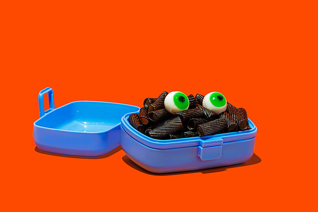 Horror-Lunch mit schwarzen Nudeln und Augen in Lunchbox auf orangem Hintergrund