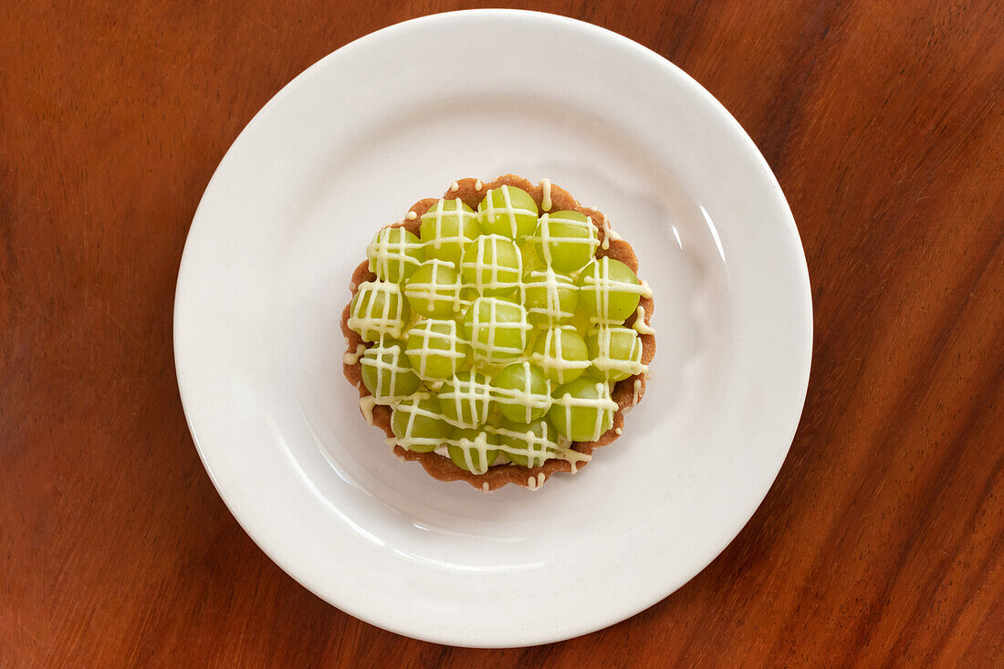 Draufsicht auf ein appetitliches Matcha-Kuchendessert mit grüner Sahne auf einem weißen Teller über einem hölzernen Esstisch bei Tageslicht