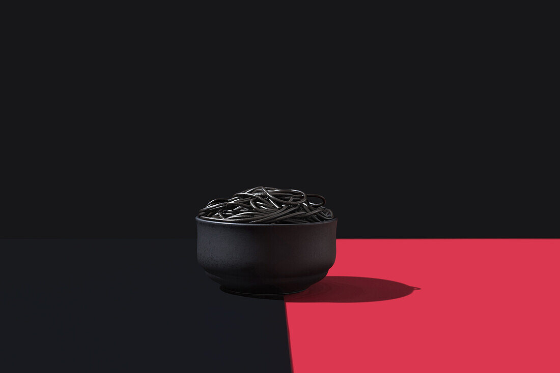 Black spaghetti in a bowl placed on black and red surface against black wall