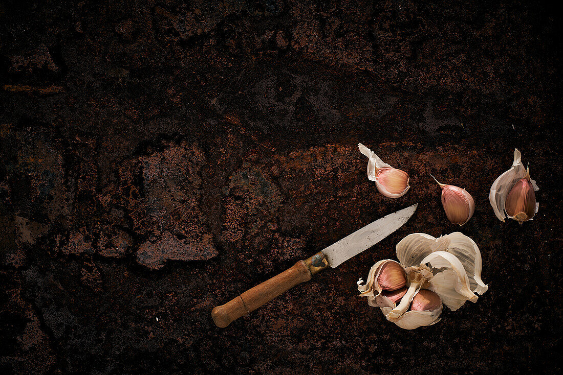 Top view of knife and half peeled garlic placed on rough rocky surface
