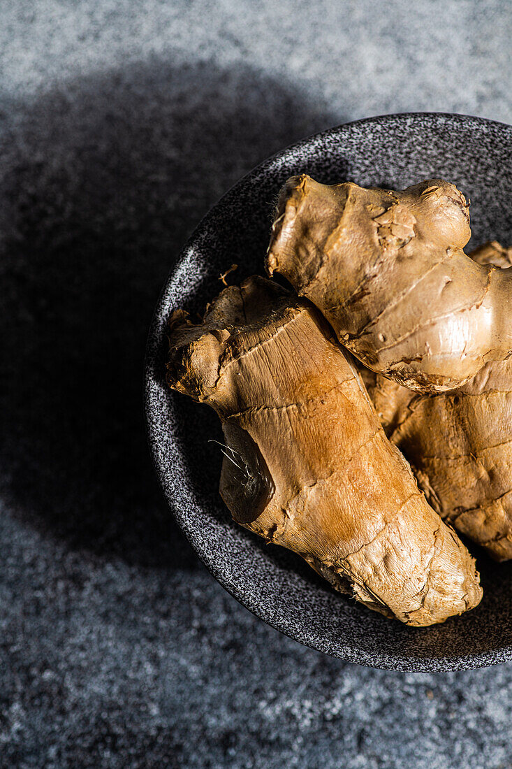 Black stone bowl with ginger roots on concrete kitchen table