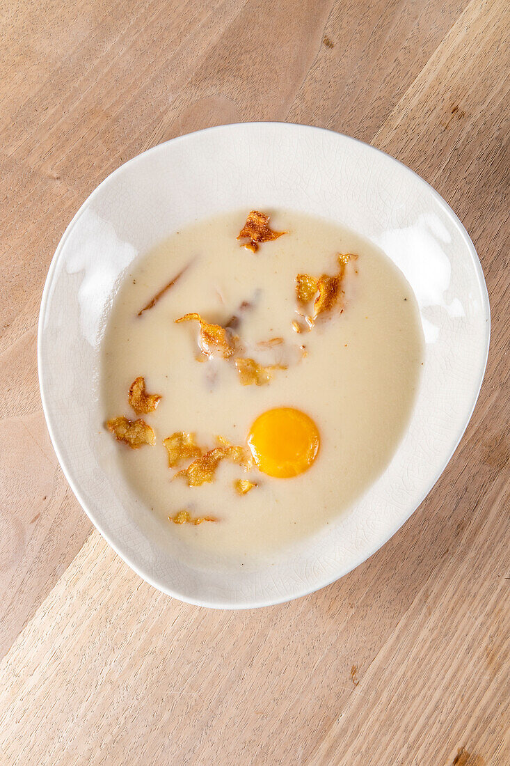 From above creamy sauce with fried strips and raw egg yolk in plate on wooden table