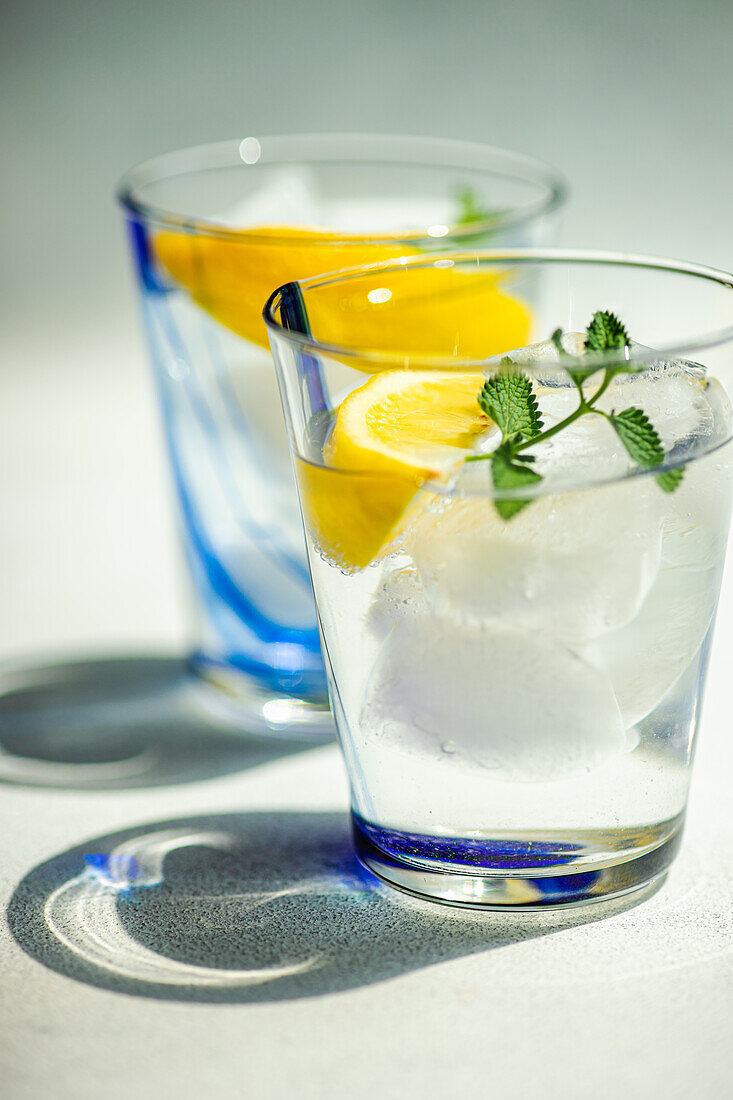 Nahaufnahme eines Sommercocktails mit Zitronenwodka, Zitronenscheiben und wilden Minzblättern, serviert mit Eis auf einem weißen Tisch