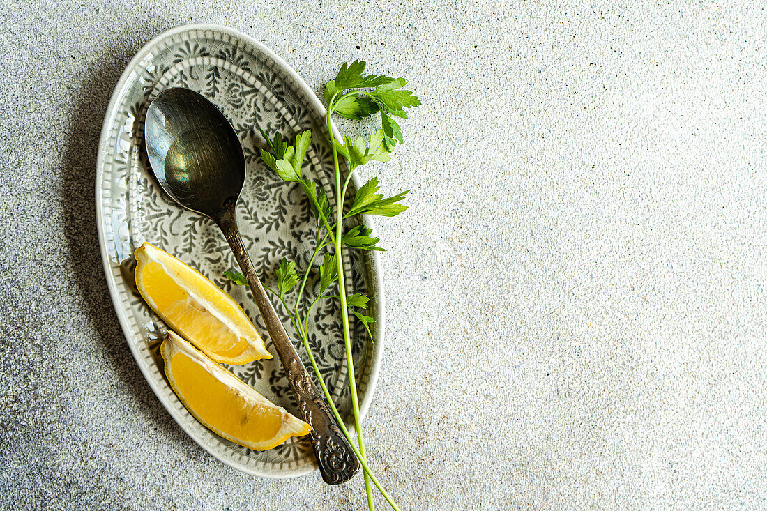 Top view of spoon with virgin olive oil, lemon slices and green parsley herb on plate against gray background