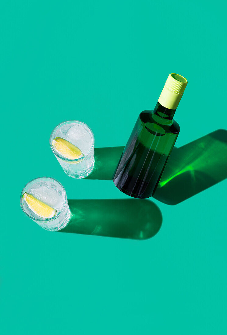 A stylish gin tonic cocktail in a glass with a slice of lime, showcased on a green backdrop with sharp shadows.