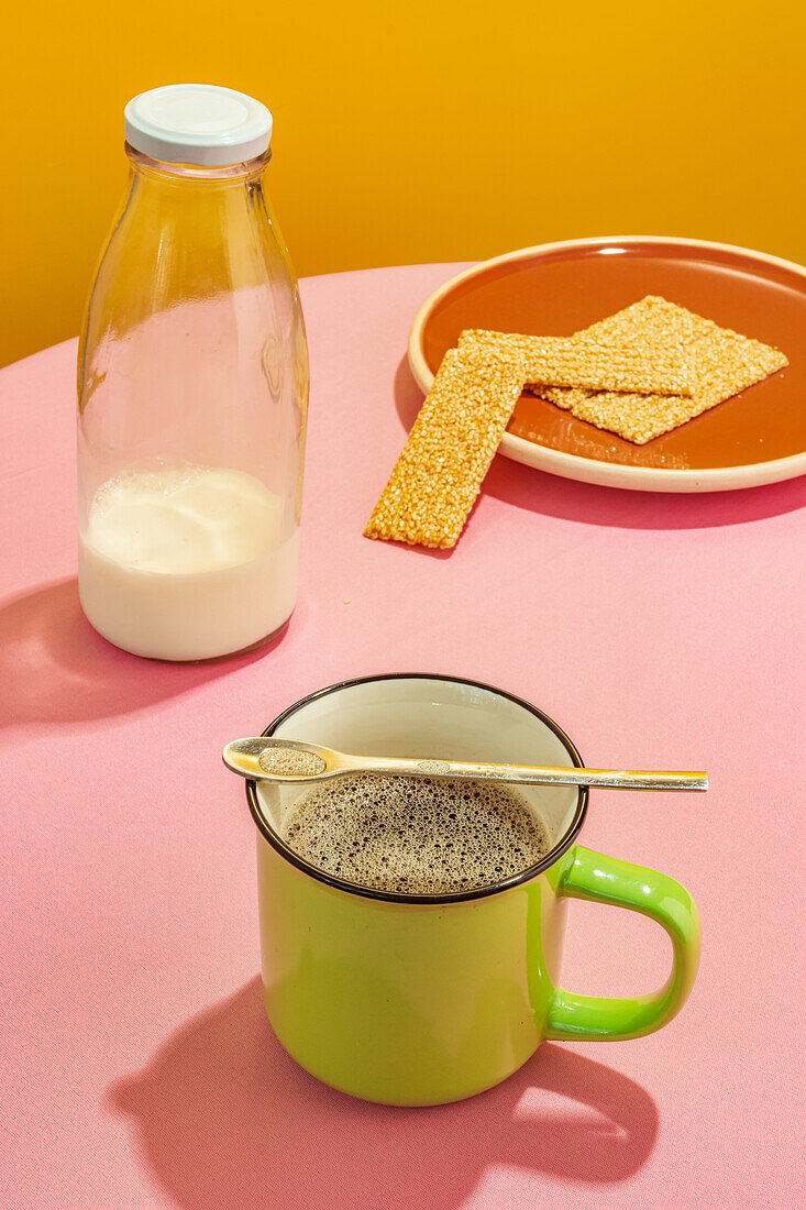 Glasflasche mit Milch und Tasse mit aromatischem Kaffee auf rosa Tisch vor gelbem Hintergrund