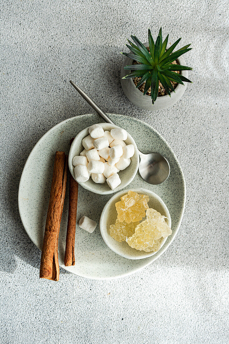 Artful arrangement of cinnamon sticks, fluffy marshmallows, and crystalline rock sugar, accompanied by a small potted plant