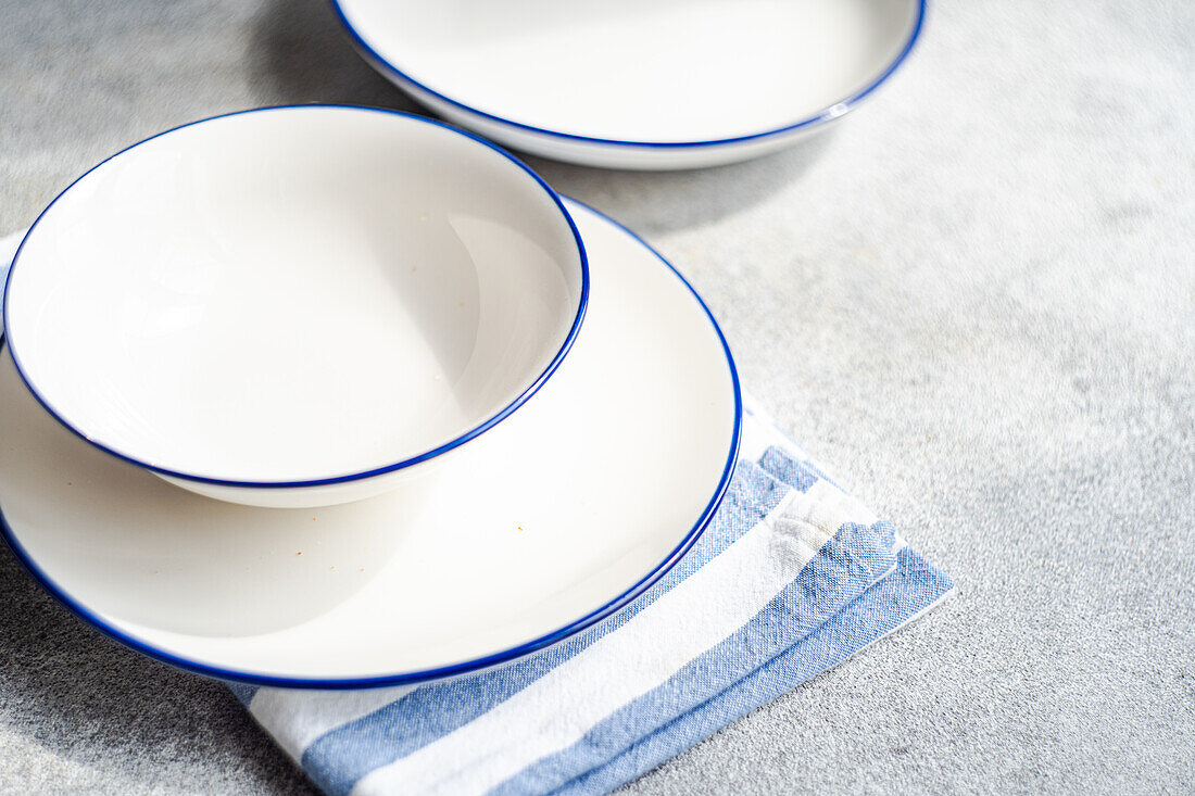 High angle of minimalistic rustic table setting with white plates and striped napkin on gray surface in daylight